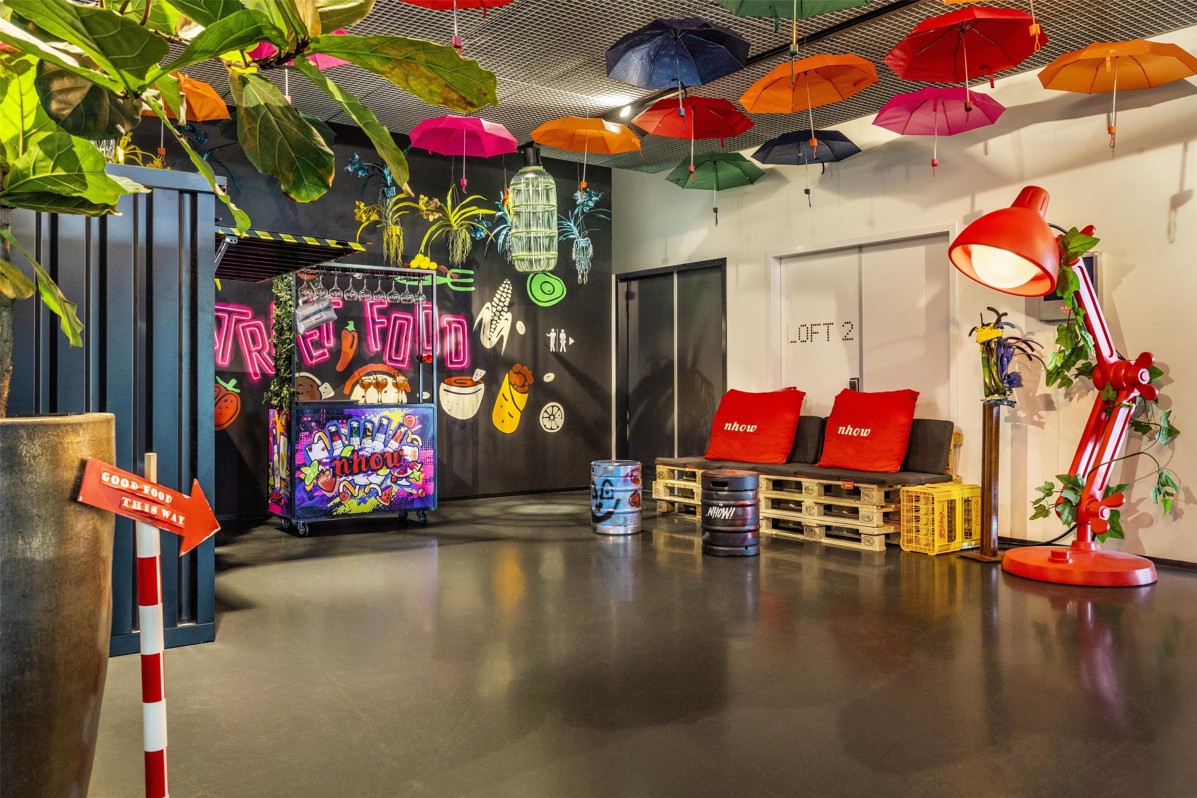Um espaço interior vibrante com guarda-sóis coloridos, um letreiro de neon e uma máquina de jogos divertida.