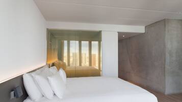 A modern hotel room with a large bed, a concrete accent wall, and a unique textured window blind.