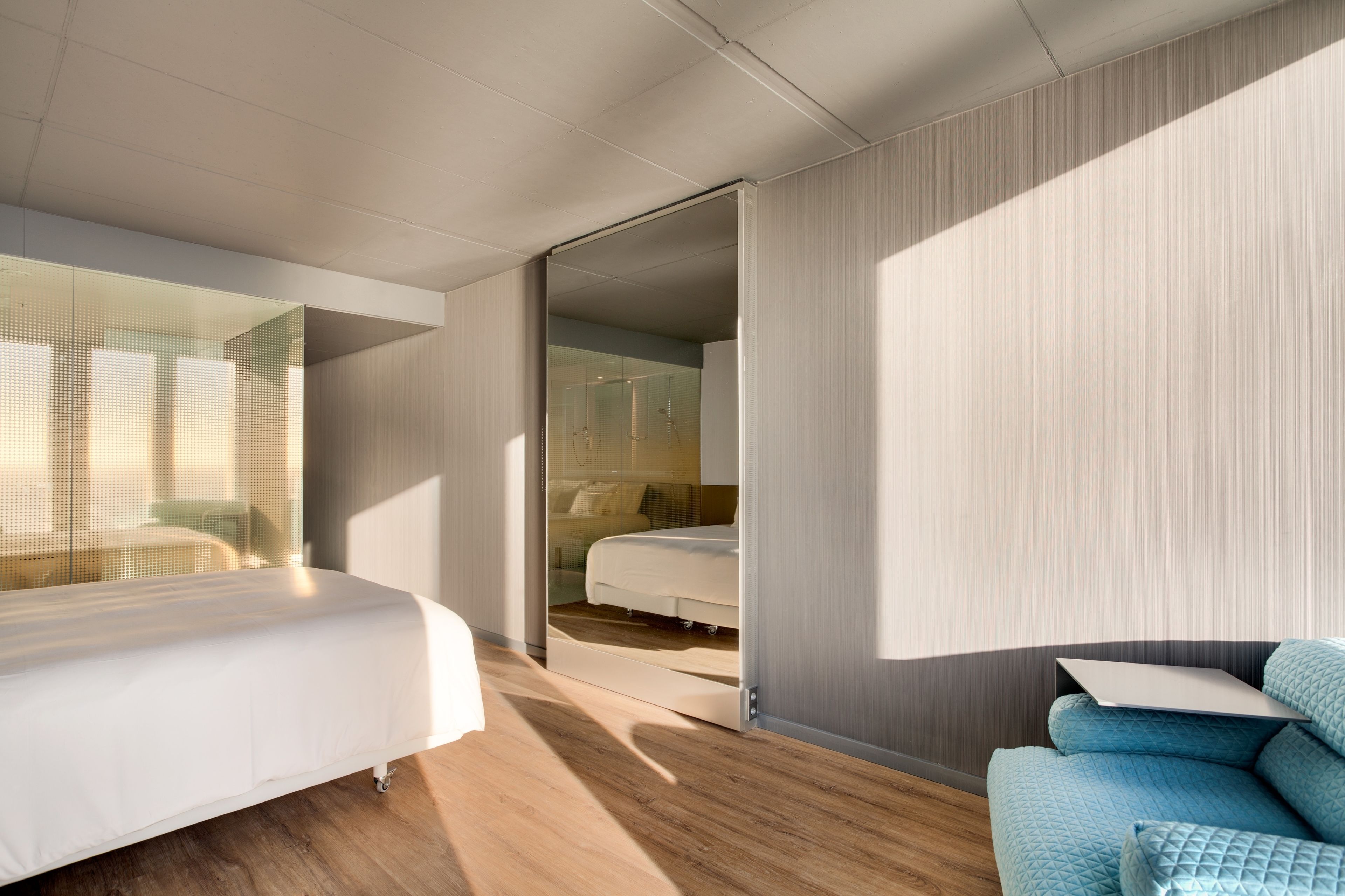 A modern hotel room with a bed, a sofa, and a glass partition.