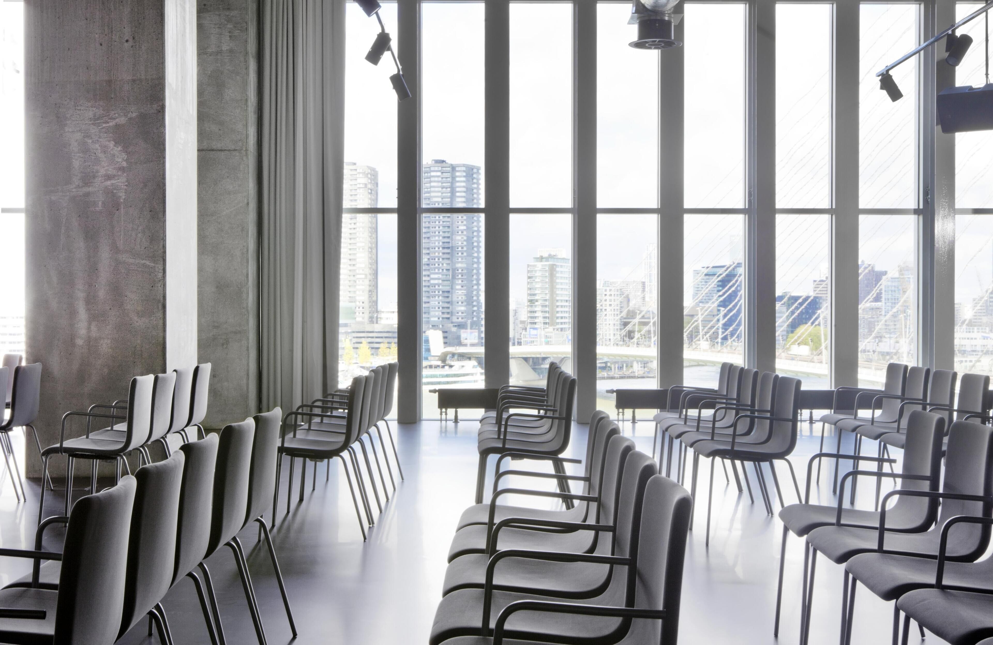 A conference room with rows of chairs and tables, large windows with a cityscape view.