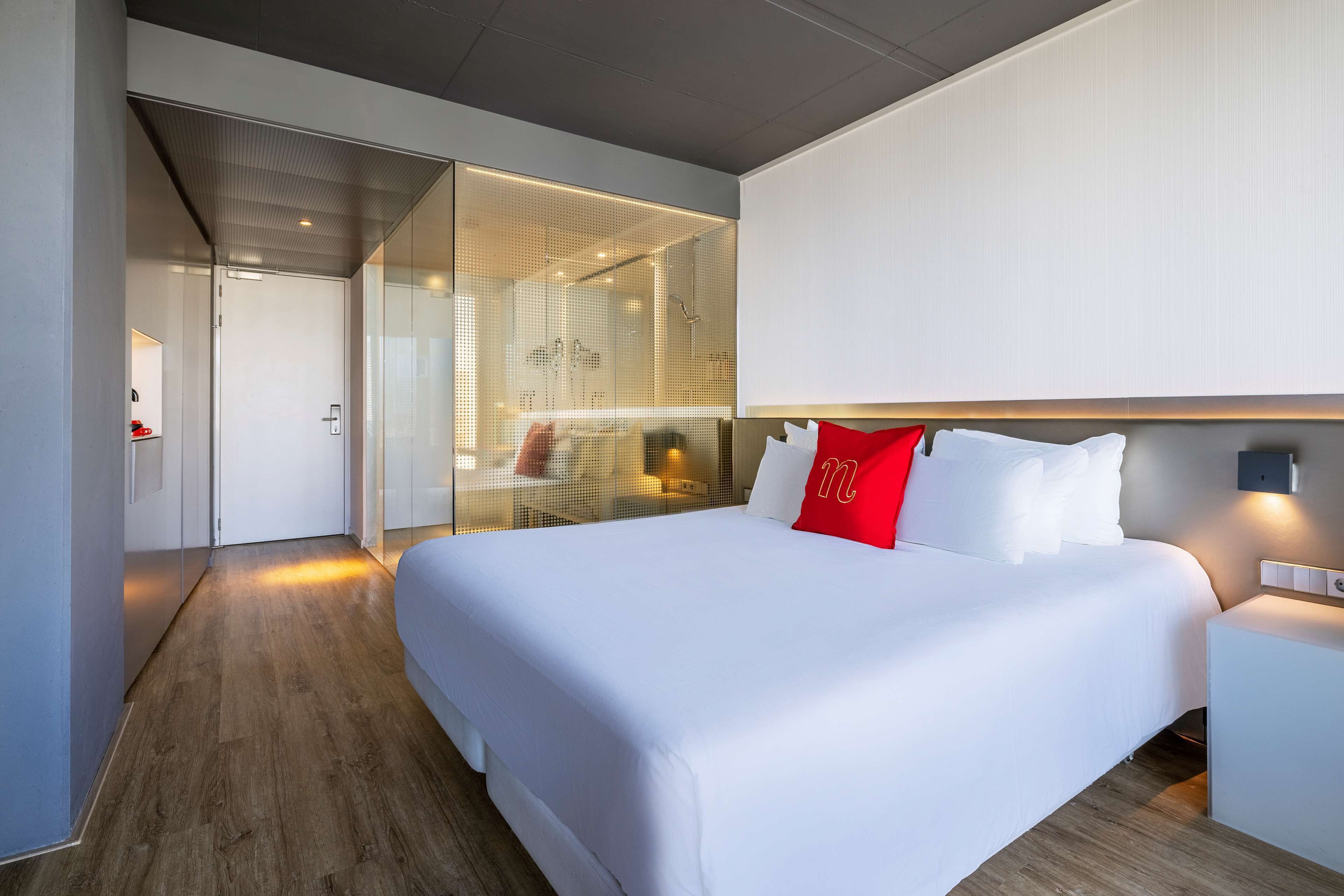 Une chambre d’hôtel moderne avec un grand lit, une cloison en verre et un plancher en bois.