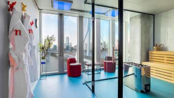 A modern hotel room with large windows, a city view, red seating, and a trash bin.