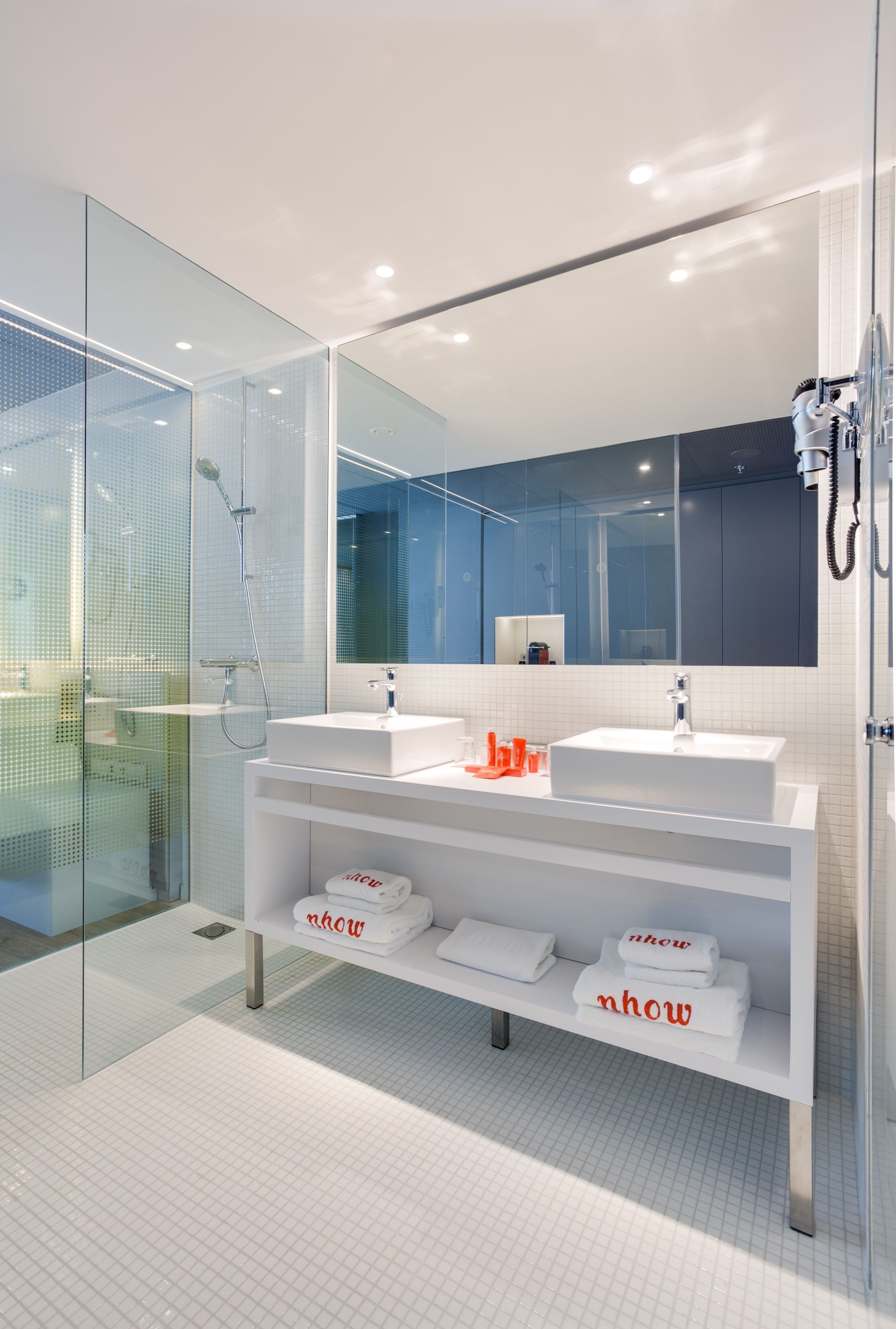 A modern bathroom with a glass shower enclosure, two sinks, a large mirror, and a white vanity with towels.