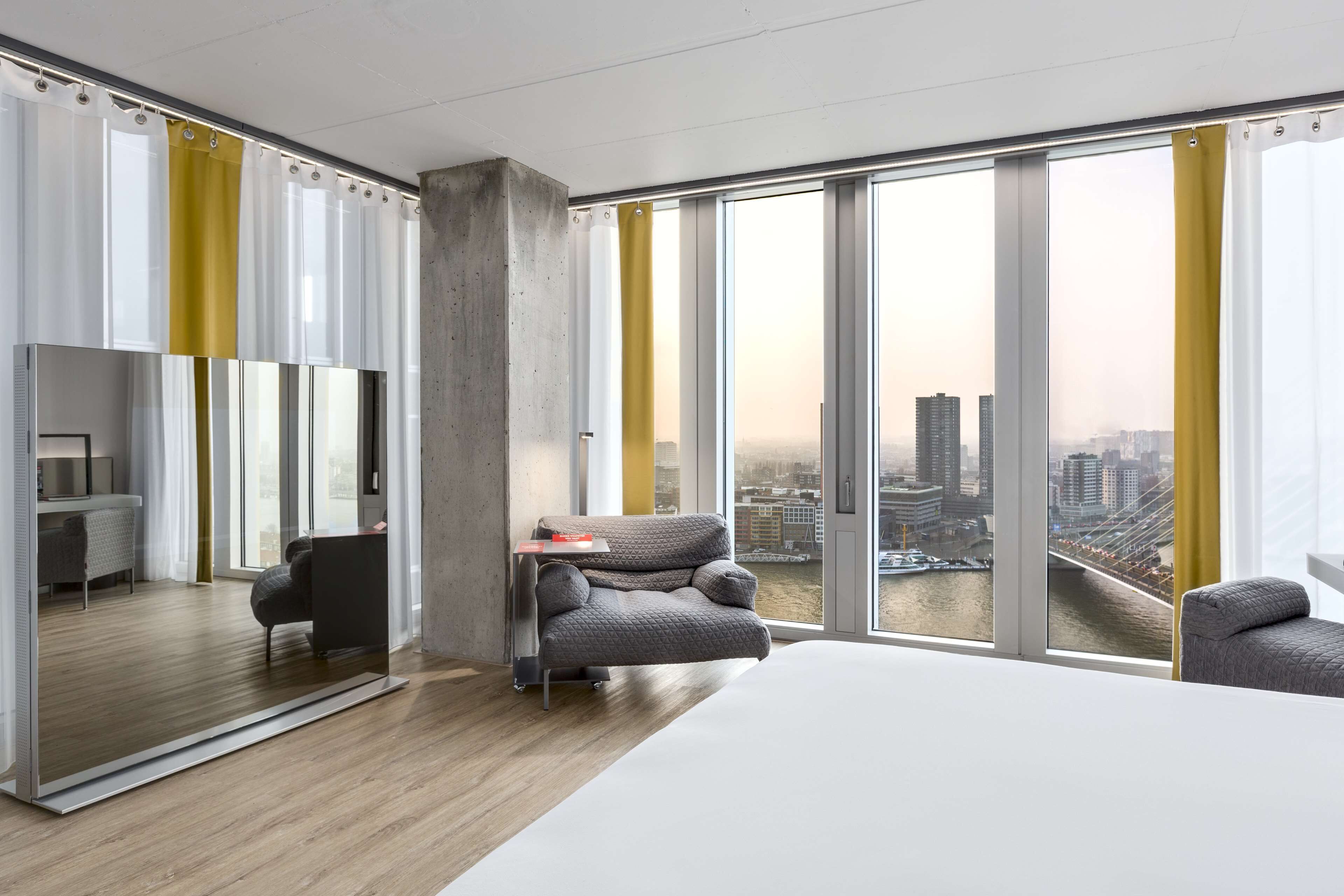 Habitació d'hotel moderna amb un llit gran, zona de seients amb un sofà i una butaca, escriptori i un finestra gran amb vista a la ciutat.