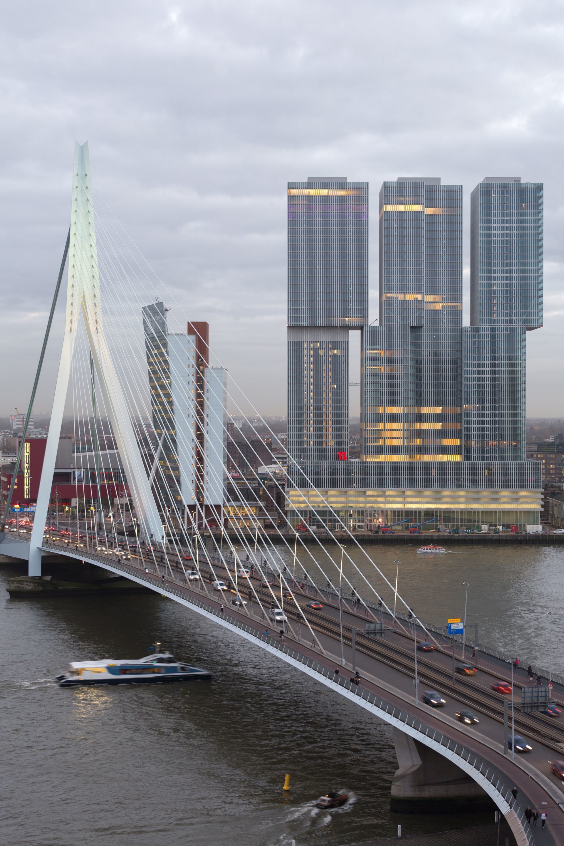 Un puente atirantado con una pasarela peatonal y una carretera que cruza un río, con edificios modernos al fondo.