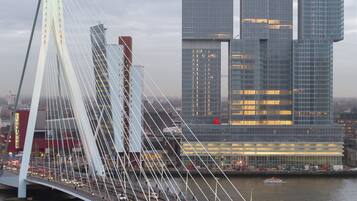Un puente atirantado con una pasarela peatonal y una carretera que cruza un río, con edificios modernos al fondo.