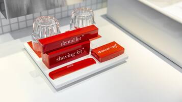 Un baño con encimera blanca, un portalápices rojo, un afeitor rojo y un peine rojo.