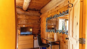 A wooden cabin interior with a television on a dresser, a desk with a chair, and a large mirror on the wall. - Auberge Couleurs de France (Duhamel)