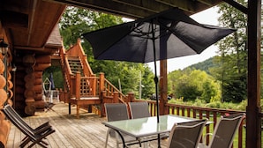 A wooden deck with a glass table and chairs, a black umbrella, and a wooden staircase. - Auberge Couleurs de France (Duhamel)