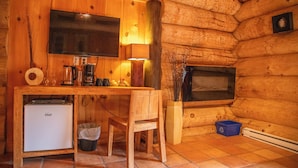 A compact kitchen with wooden walls, a TV mounted above the counter, a small fridge, and a chair. - Auberge Couleurs de France (Duhamel)