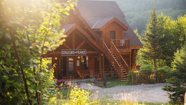 A wooden lodge with a sign reading "COULEURS de FRANCE" and a staircase leading to a balcony. - Auberge Couleurs de France (Duhamel)