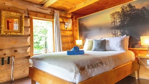A wooden cabin bedroom with a bed, a nightstand, a wall-mounted fan, a window with curtains, and a framed picture. - Auberge Couleurs de France (Duhamel)