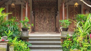 A traditional building entrance with a large ornate door, potted plants, and a tiled roof. -  Puri Saraswati Dijiwa Ubud (Ubud)