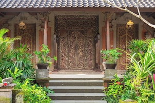Uma fachada tradicional de edifício com uma porta grande e ornamentada, plantas em vasos e telhado telhado.