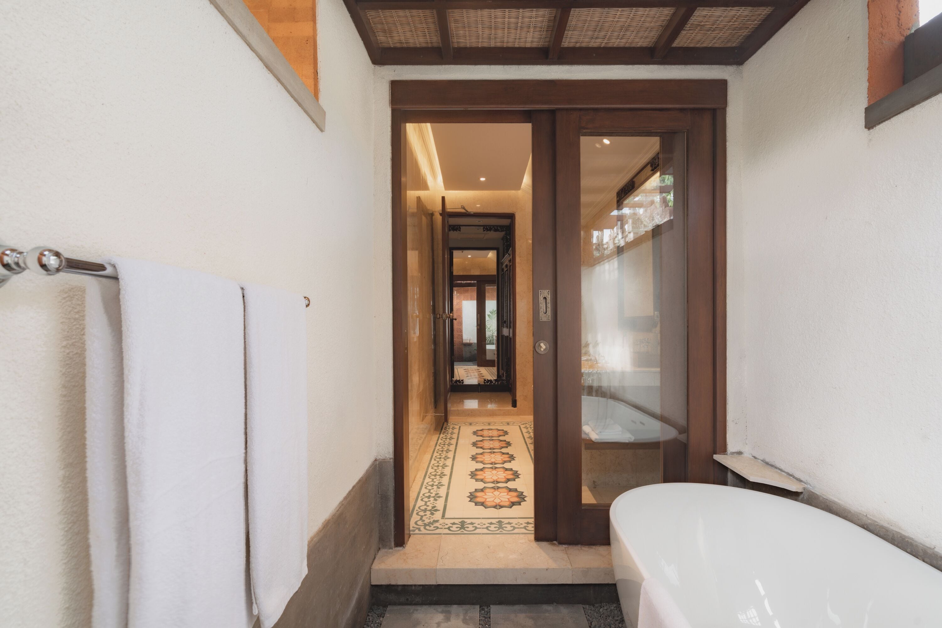 Un couloir étroit, dont le sol est orné de motifs, mène à une pièce où se trouve une baignoire.