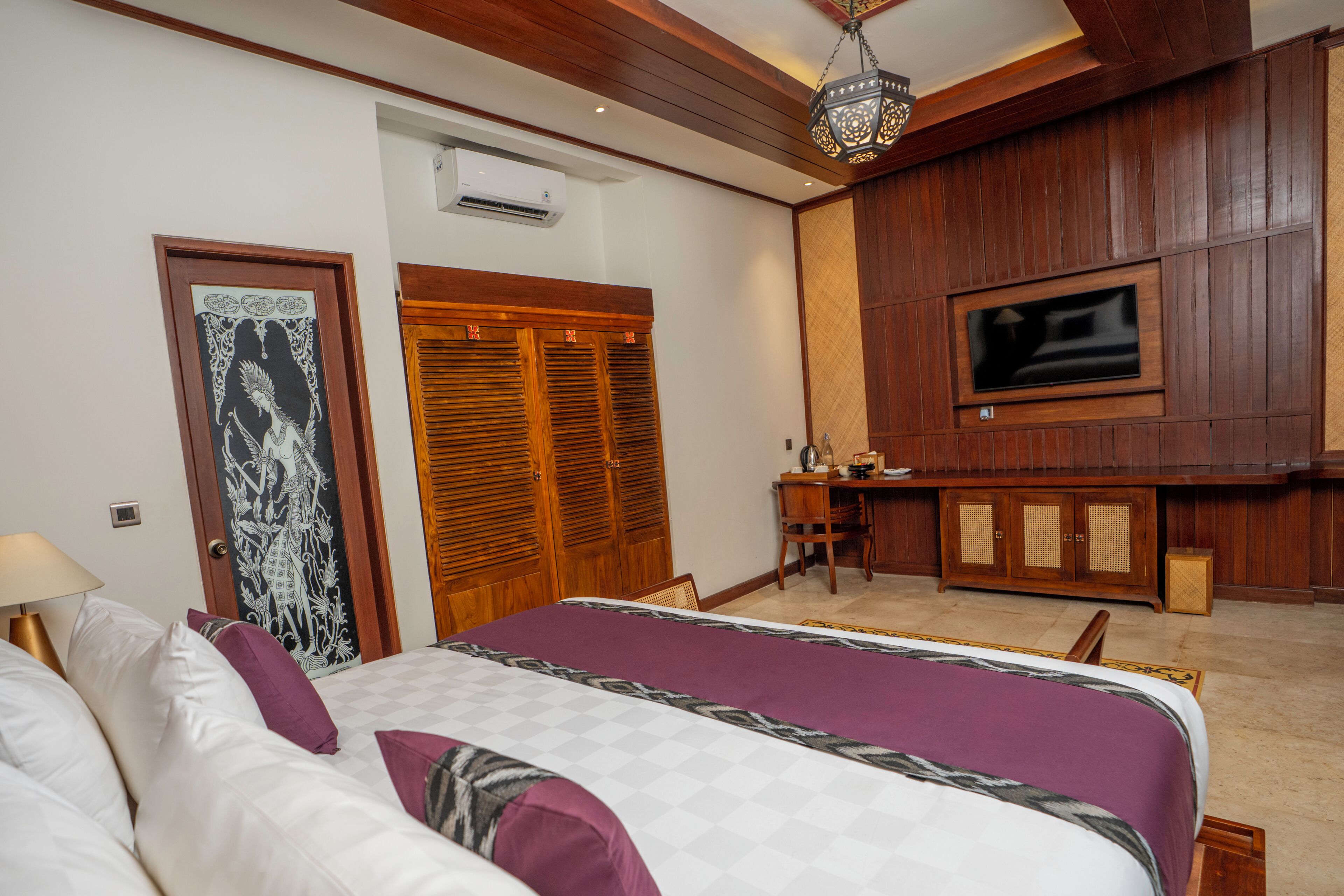 A bedroom with a large bed, wooden wardrobe, desk, and a television mounted on the wall.