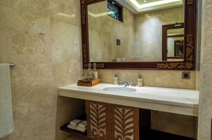 A bathroom with a marble wall, a large mirror, a sink, and a cabinet with decorative patterns.