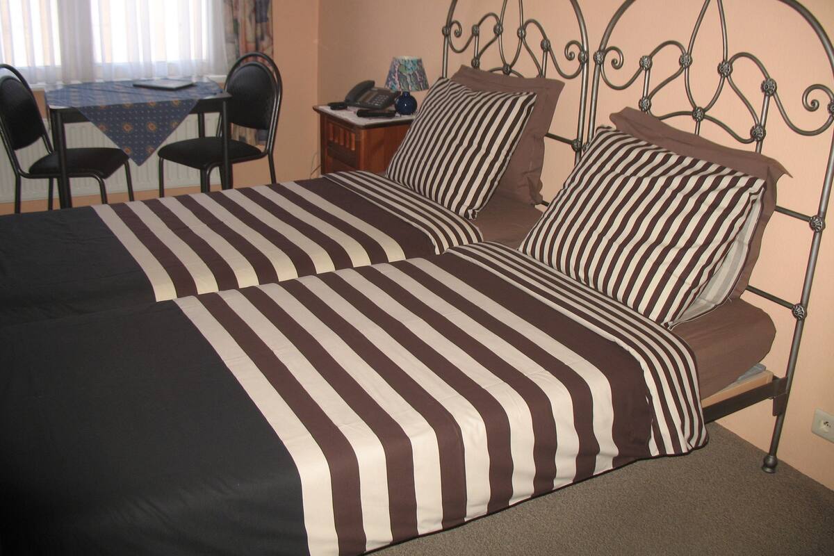A bed with striped bedding, a bedside table with a lamp, and a chair.