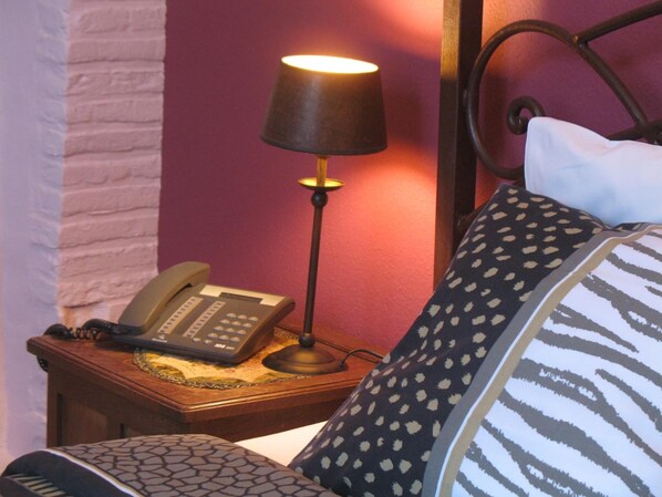 A bed with patterned pillows, a bedside lamp, and a telephone on a wooden nightstand. - B&B Het Wit Beertje (Bruges)