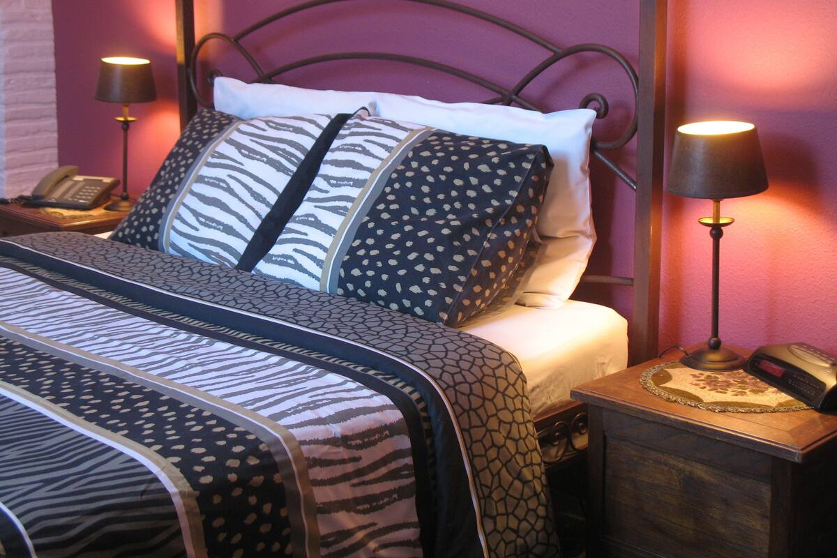 A neatly made bed with patterned bedding, a bedside telephone, and two wall-mounted lamps.