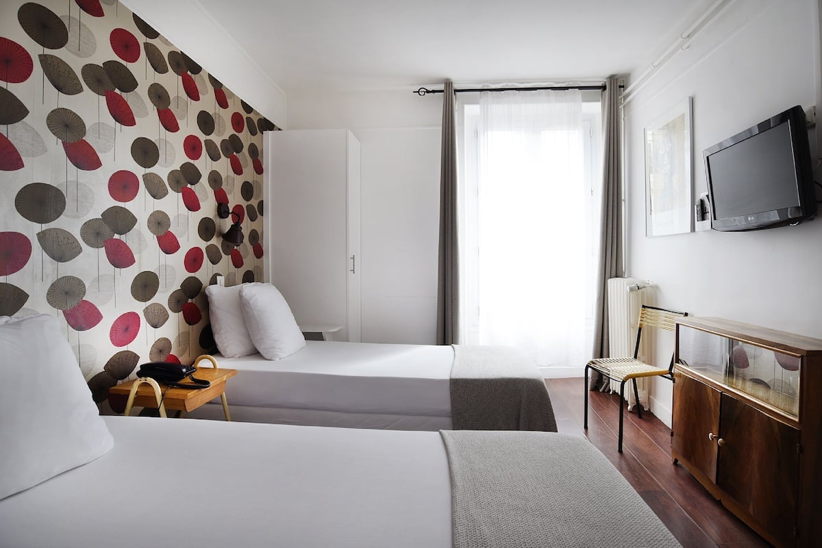 Hotellihuone, jossa on kaksi sänkyä, työpöytä lampun kanssa, tuoli, televisio ja vaatekaappi.