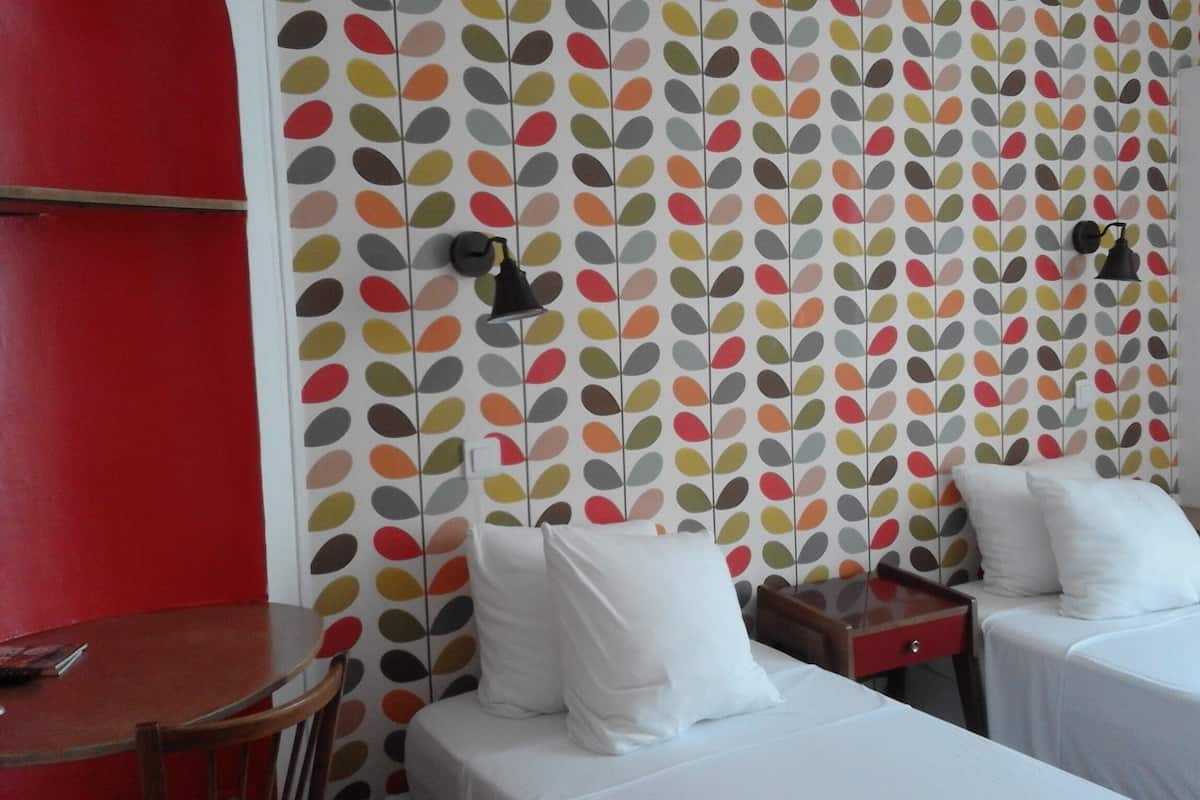 Hotellihuone, jossa on kaksi sänkyä, punainen seinä ja lehtikuviollinen tapetti.