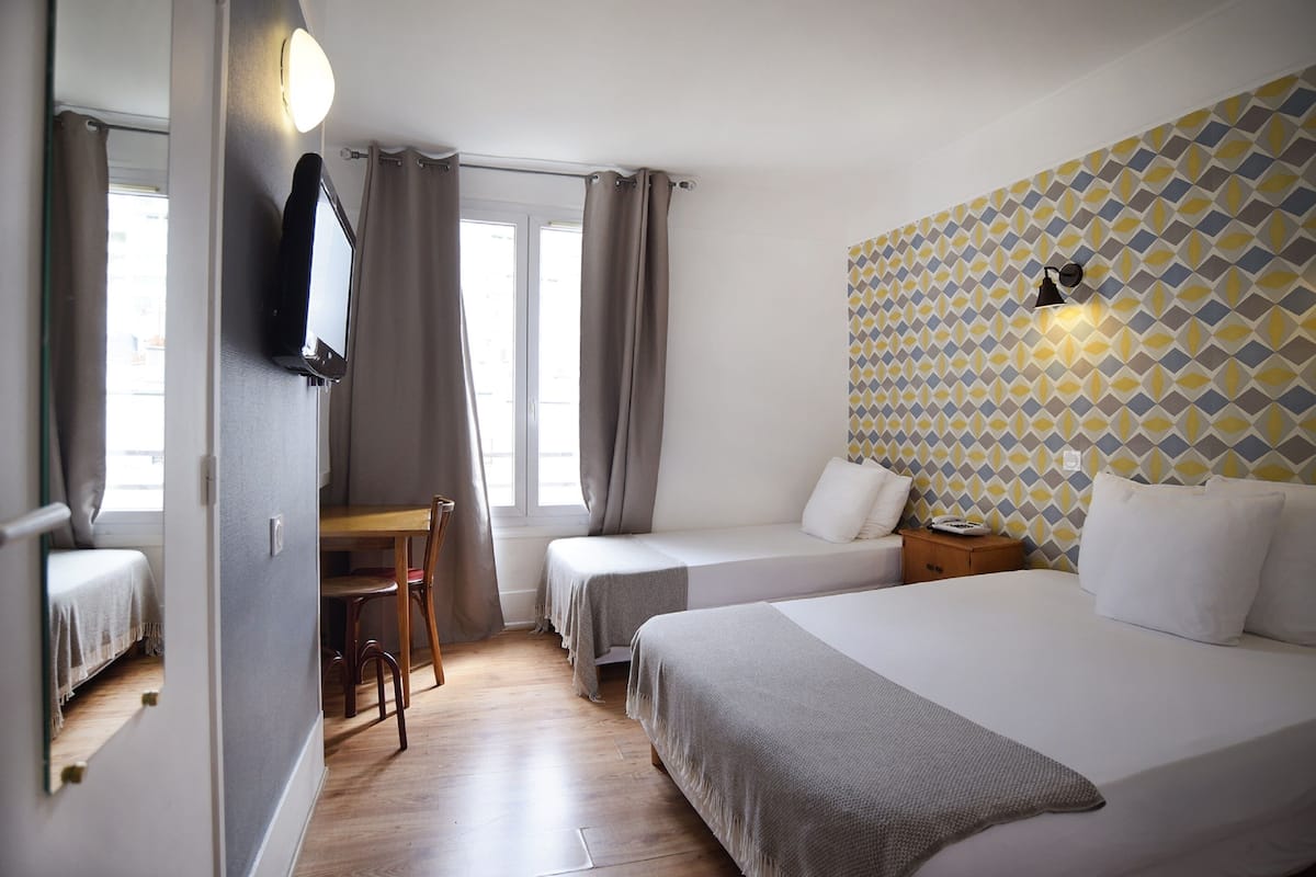 Hotellihuone, jossa on kaksi erillistä sänkyä, työpöytä, tuoli, pieni pöytä ja seinään kiinnitetty valaisin.