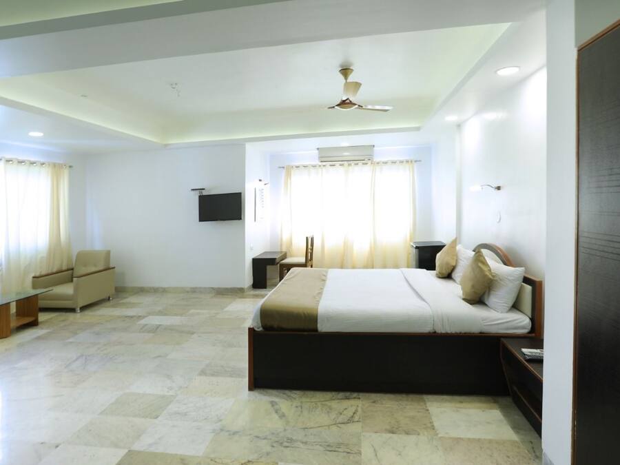 A bedroom with a bed, a chair, a TV, and a ceiling fan.