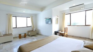 Camera d'albergo con un letto grande, una scrivania, una sedia, una TV e due finestre con tende.