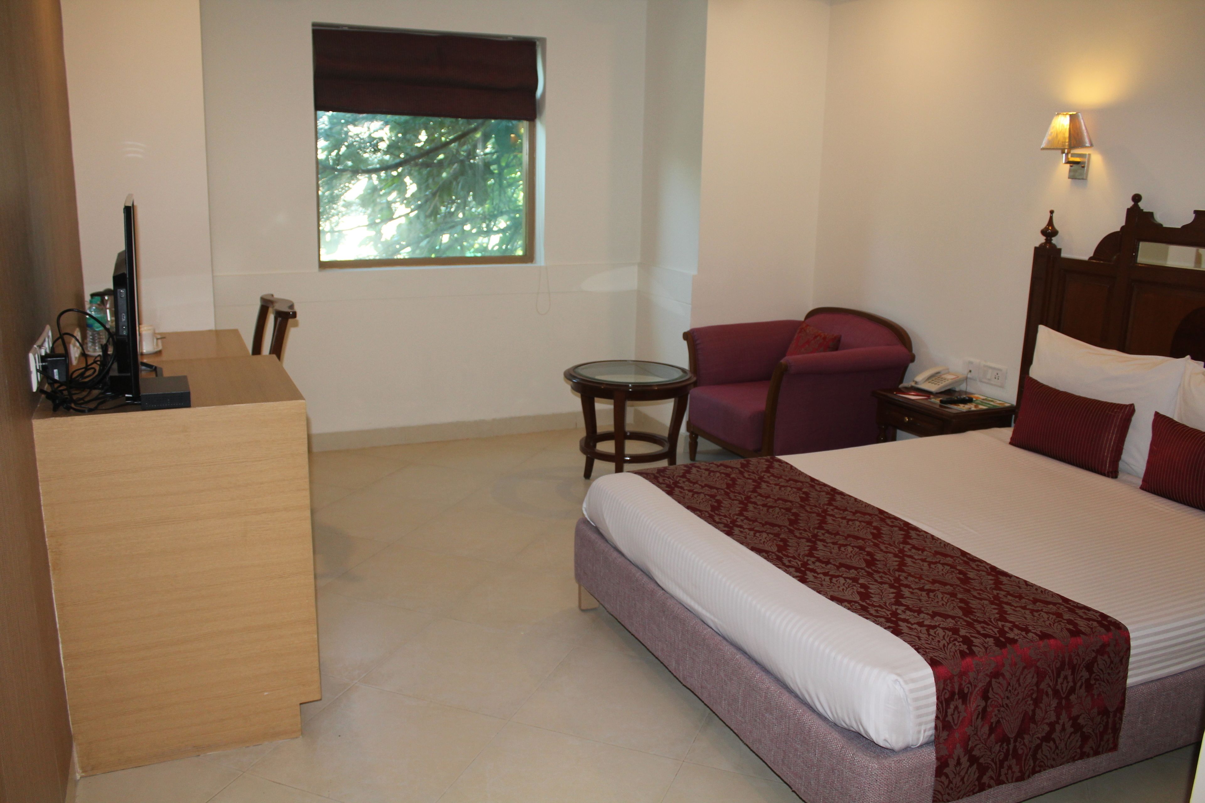 A hotel room with a bed, a desk, a chair, a small table, and a window with a view of trees.