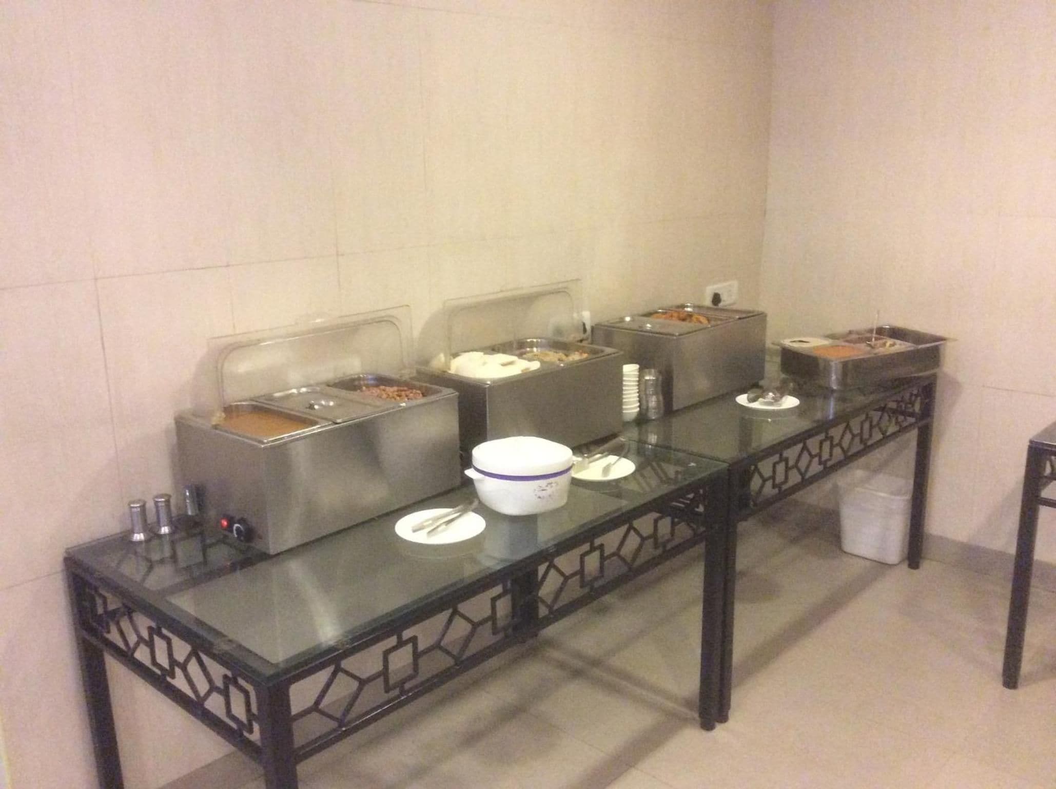 A buffet setup with multiple food dispensers, a glass table, and a trash bin.
