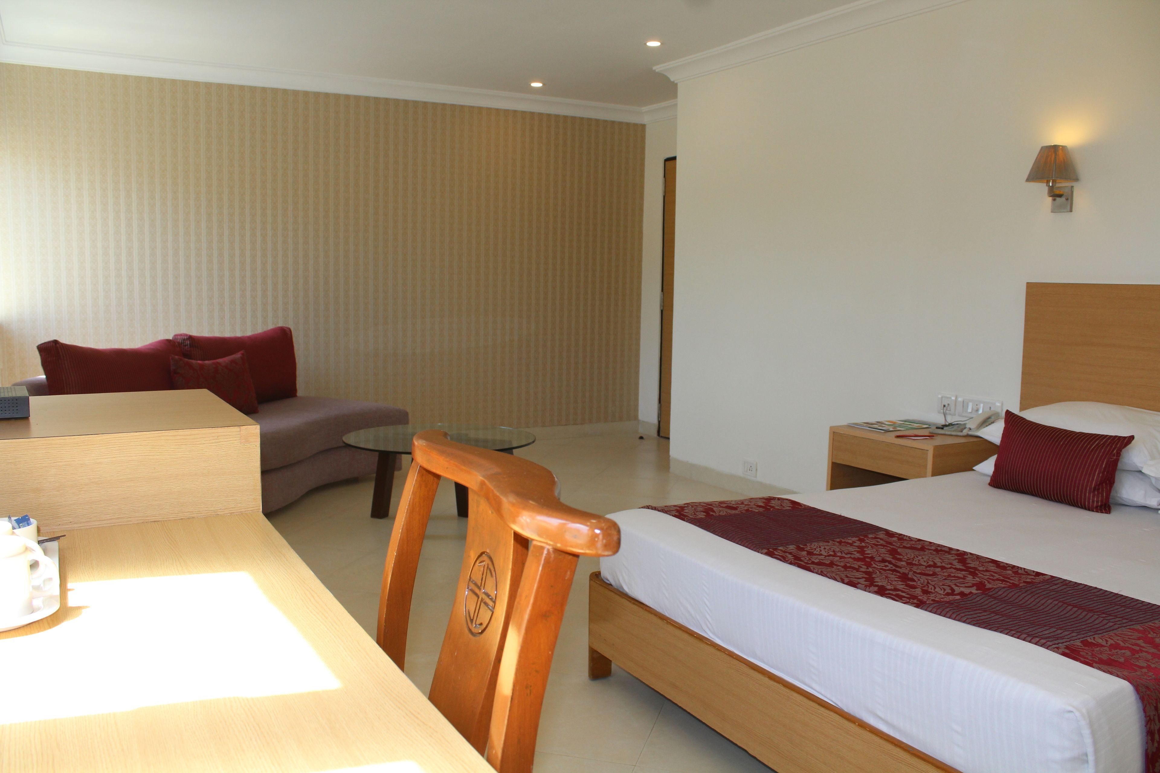 Quarto de hotel com cama, escrivaninha, cadeira, mesinha e sofá.