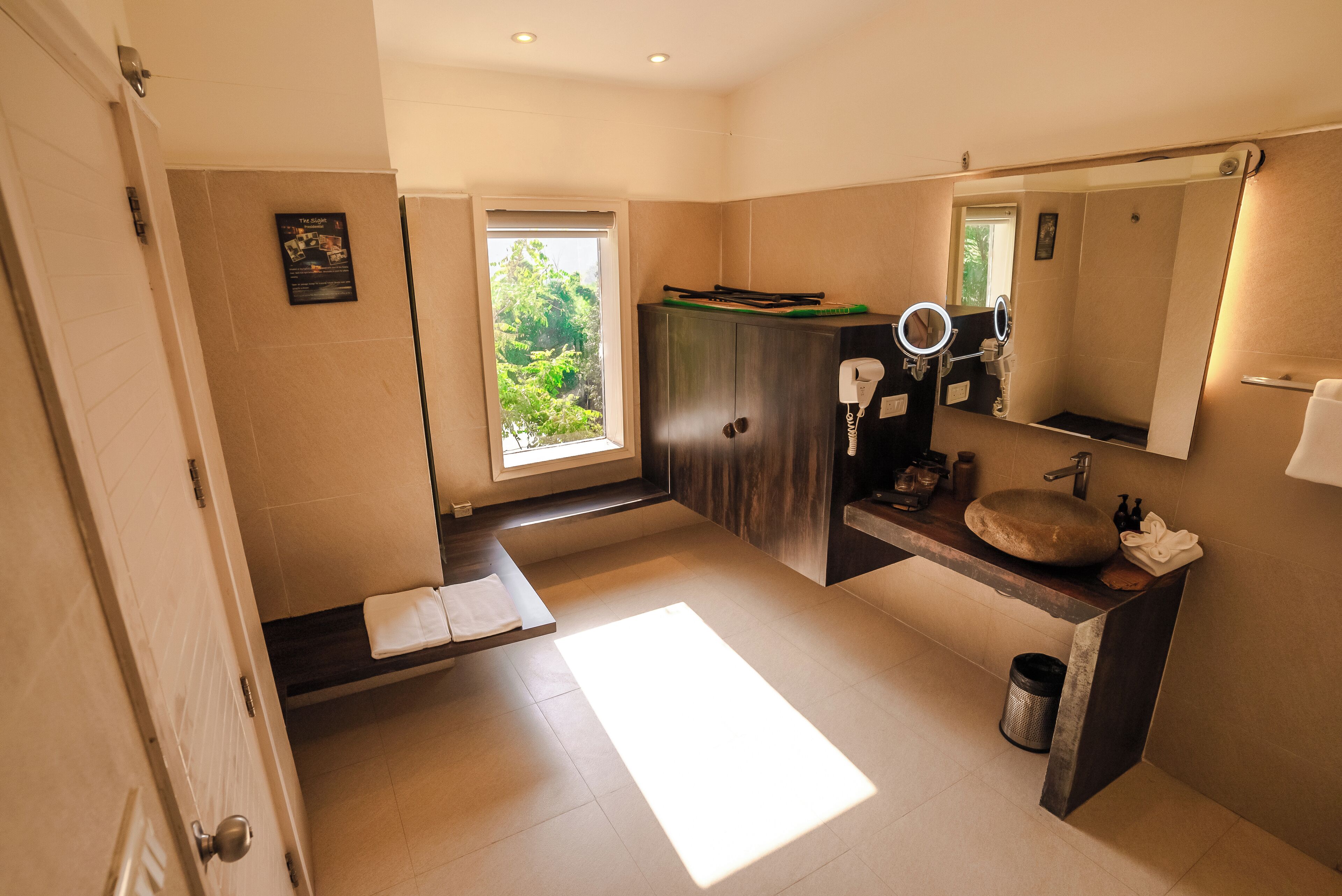 Ein modernes Badezimmer mit großem Fenster, einem Waschtisch mit rundem Spiegel und einem Handtuchhalter.