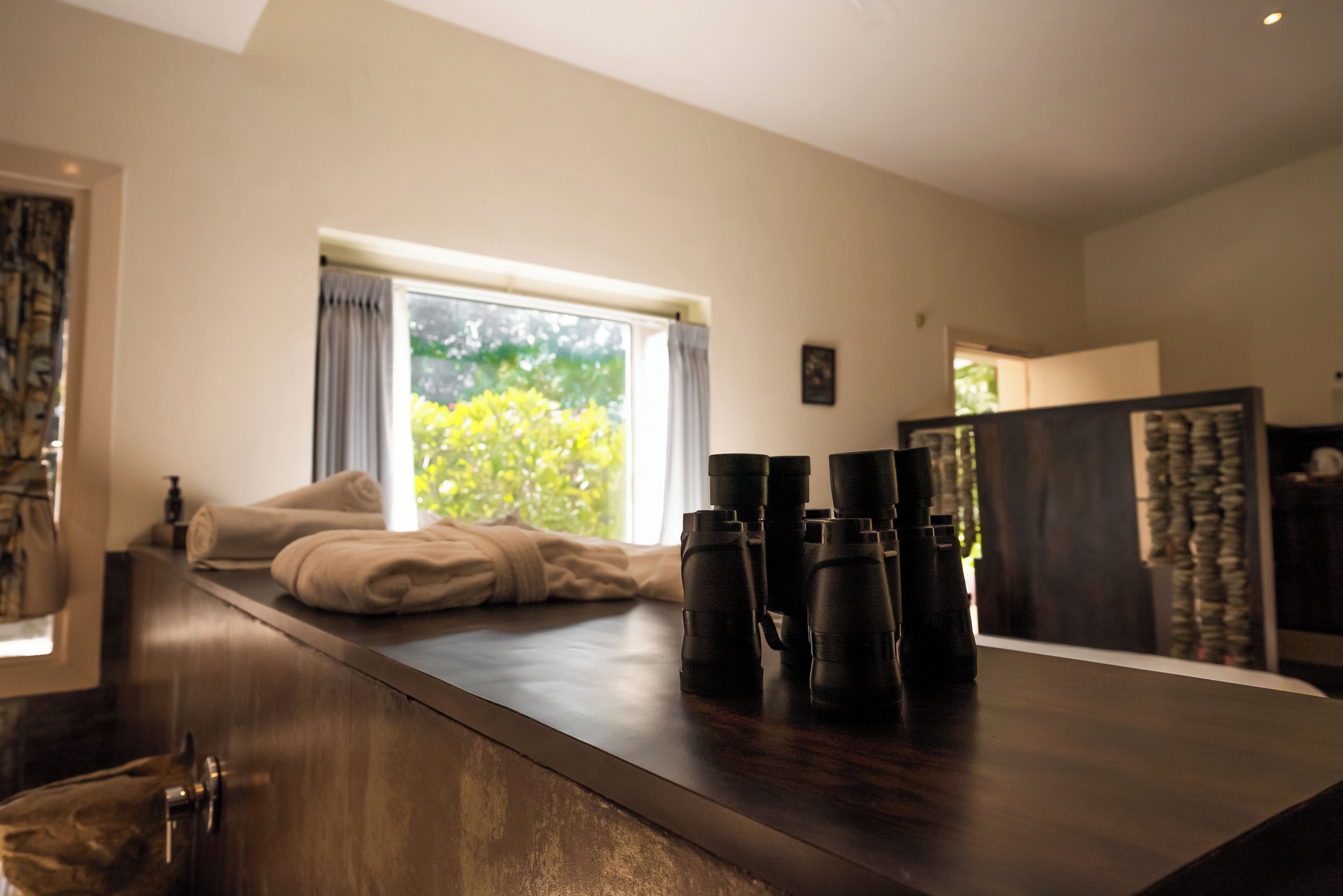 Una habitación con escritorio de madera, ventana con cortinas y vista a zonas verdes.