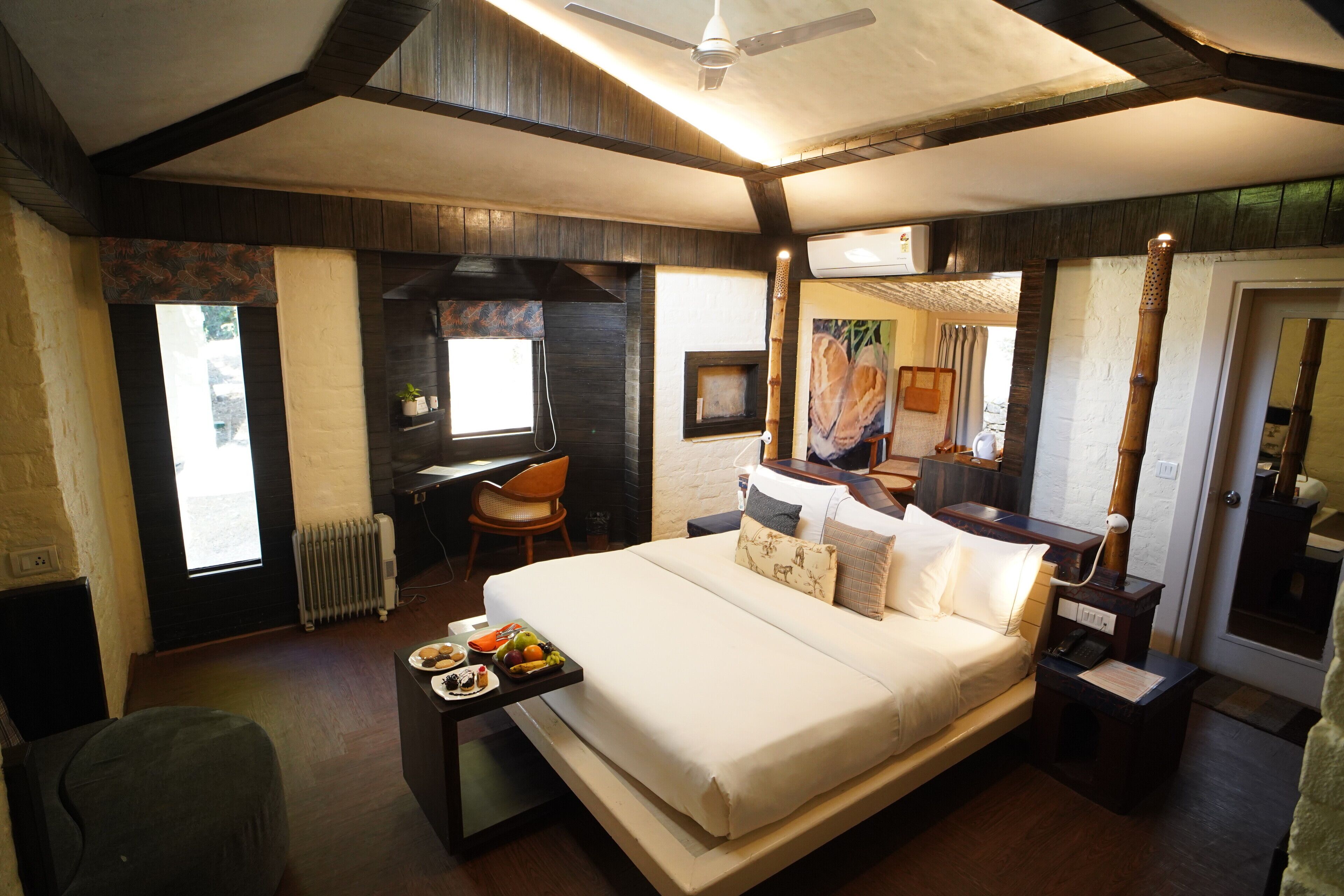 A modern hotel room with a large bed, a desk, and a chair. There is a window, a radiator, and a mirror on the wall.
