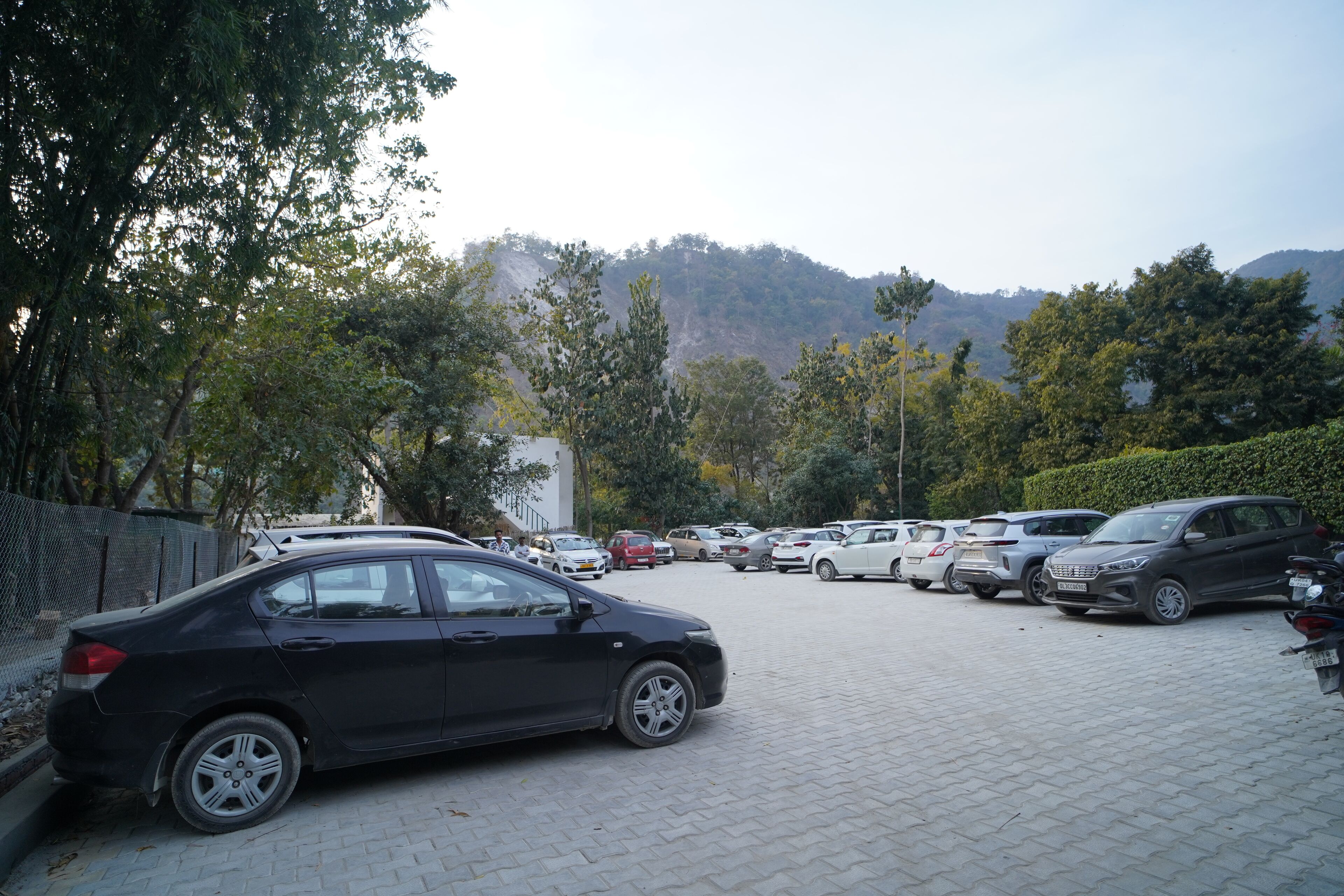 Un estacionamiento con varios autos, rodeado de árboles y un paisaje montañoso al fondo.
