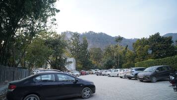 Un estacionamiento con varios autos, rodeado de árboles y un paisaje montañoso al fondo.