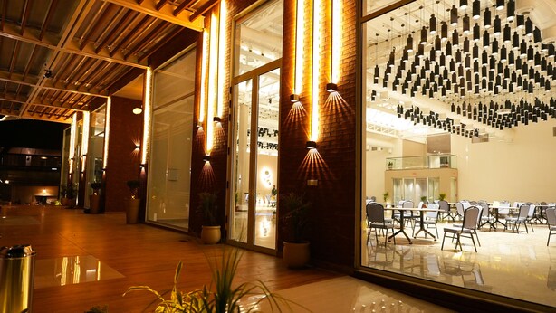 Un hall d’hôtel moderne avec un mur en verre, des plantes en pot et un espace détente avec des tables et des chaises.