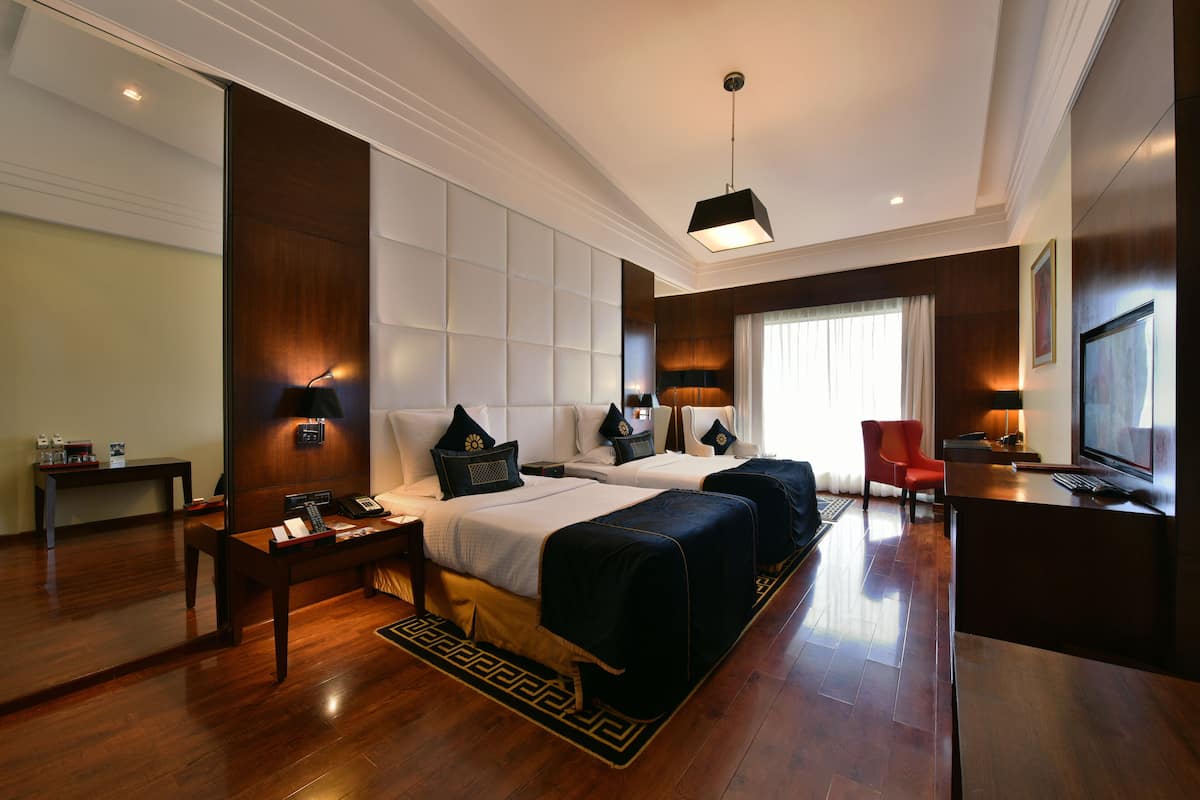Quarto de hotel com duas camas, uma escrivaninha, televisão e uma cadeira vermelha.