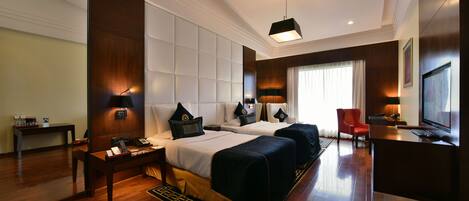 A hotel room with two beds, a desk, a TV, and a red chair.