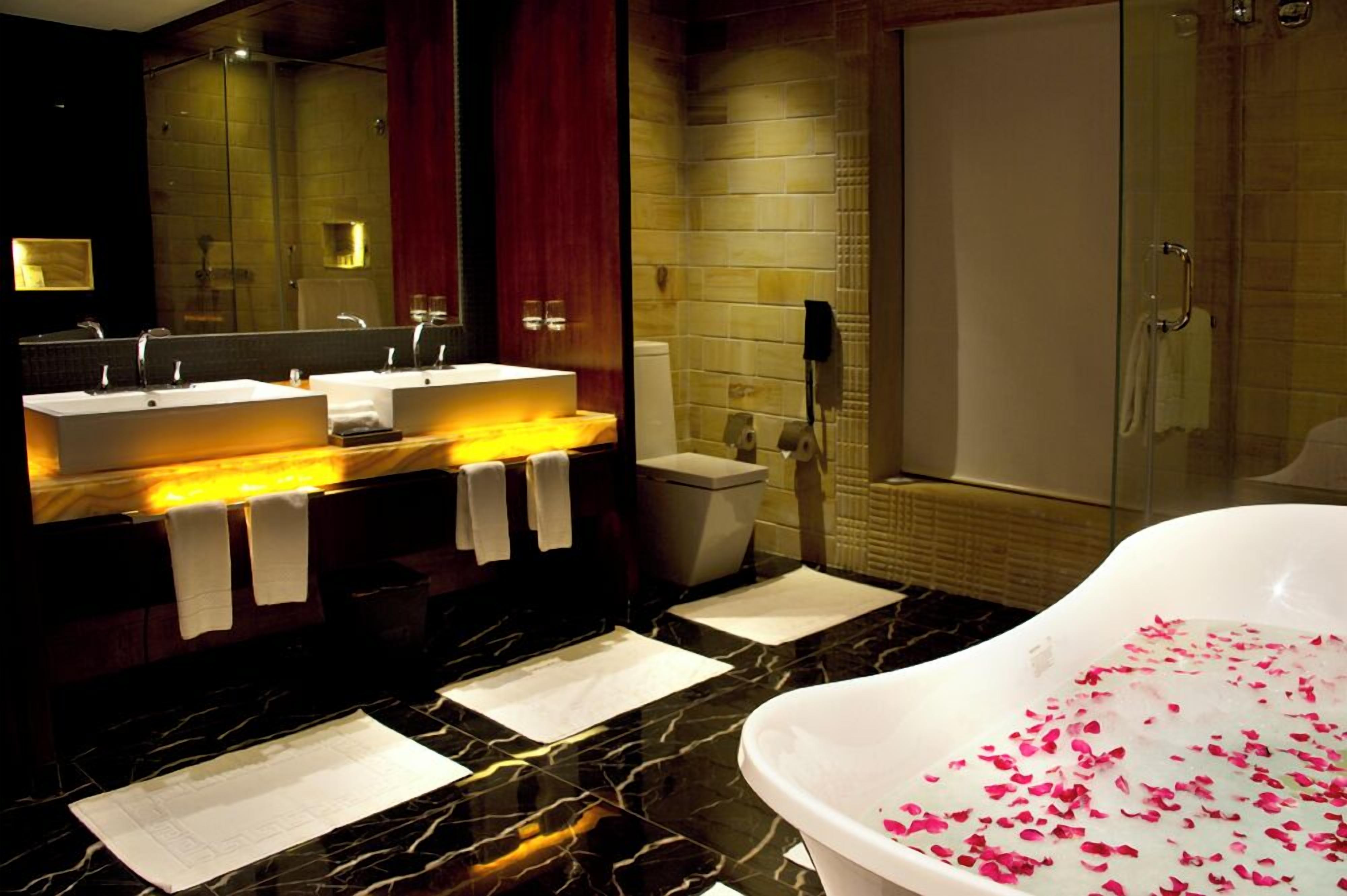 Un baño moderno con un espejo grande, dos lavamanos, una bañera con pétalos de rosa y una zona de ducha.