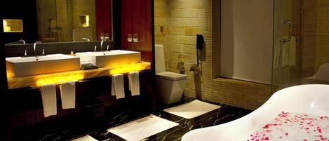 Un baño moderno con un espejo grande, dos lavamanos, una bañera con pétalos de rosa y una zona de ducha.