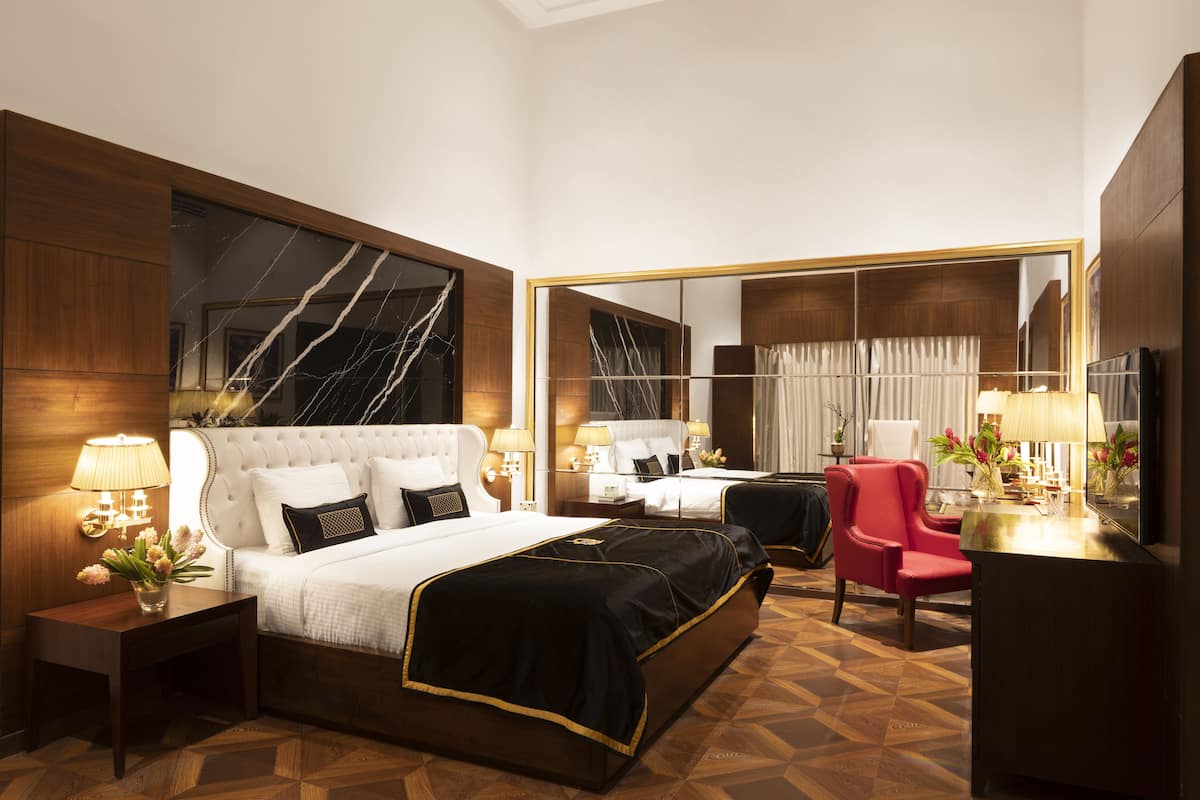 Quarto de hotel com uma cama grande, duas mesas de cabeceira, uma escrivaninha, uma cadeira e um espelho grande.