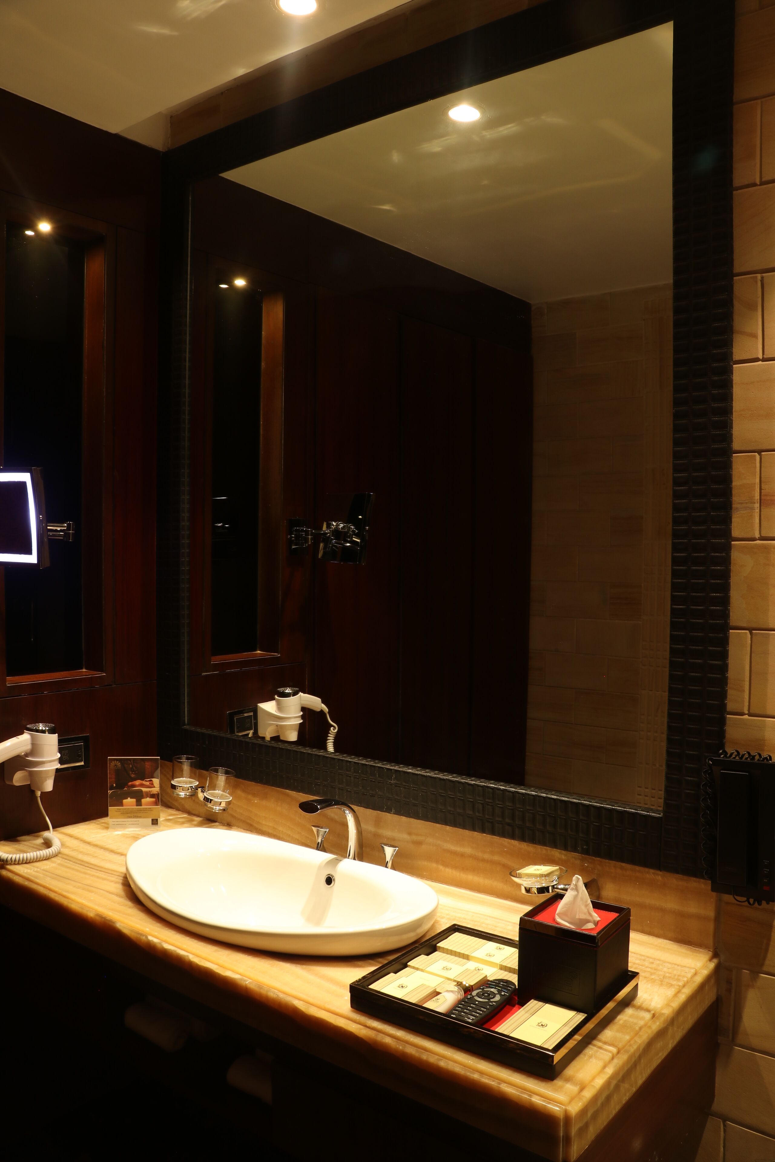 A modern bathroom with a large mirror, a white sink, and a vanity with toiletries.