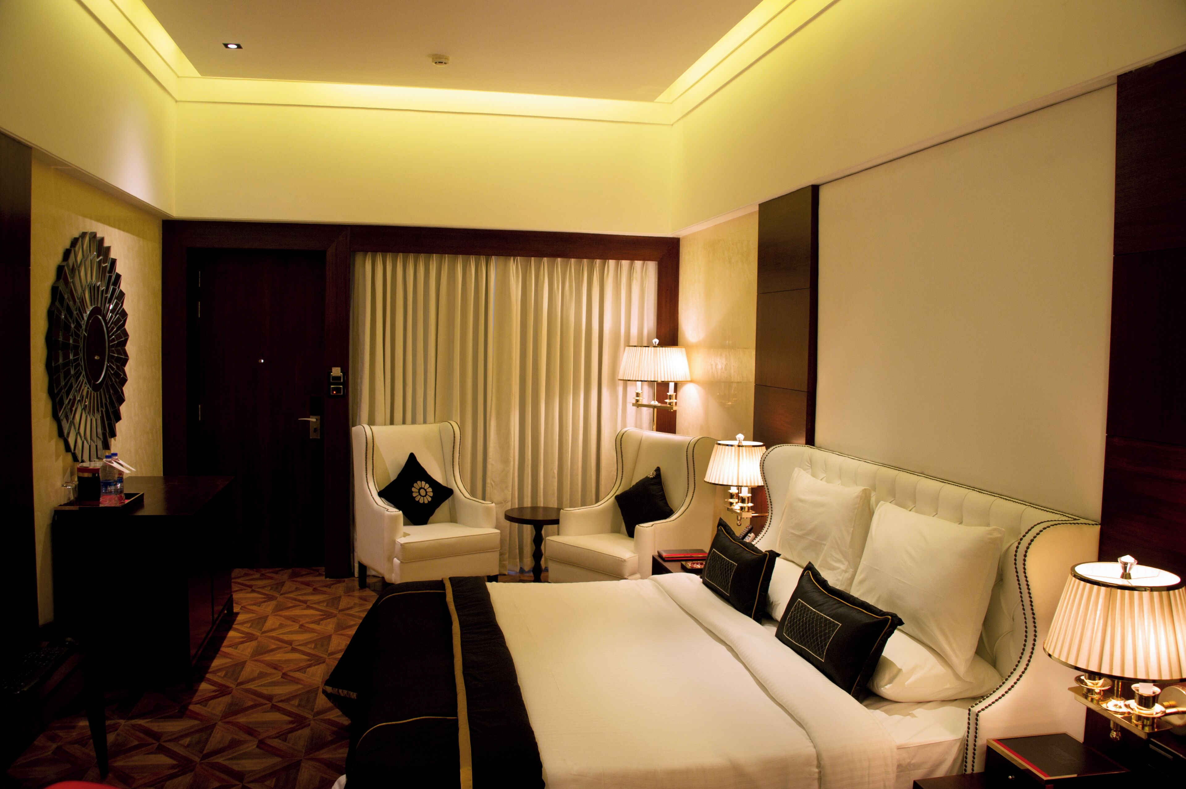 A hotel room with a large bed, two armchairs, a small table, and a lamp.