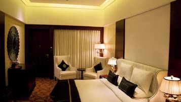 A hotel room with a large bed, two armchairs, a small table, and a lamp.