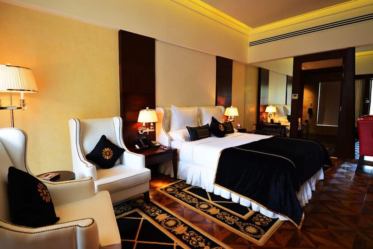 Quarto de hotel com uma cama grande, duas poltronas, uma mesa de cabeceira com abajur e um tapete estampado.
