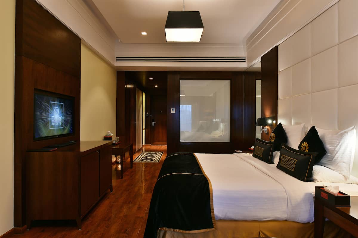 Quarto de hotel com uma cama, televisão, escrivaninha e uma janela grande.