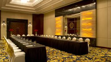 A conference room with a long table, white chairs, and a patterned carpet.