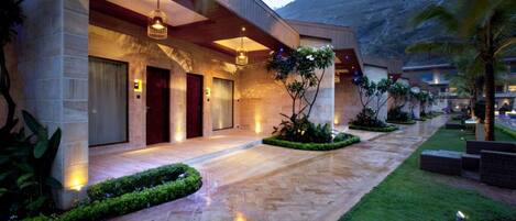 Una entrada de hotel moderna con fachada de piedra, un paseo techado y jardines bien cuidados.